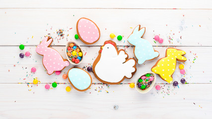 Easter greetings card with colorful gingerbread and sweets. On a white wooden background. Top view. Free space for your text.