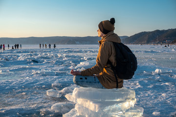 Tourist with a backpack meditates sitting in Lotus position on the ice of lake Baikal