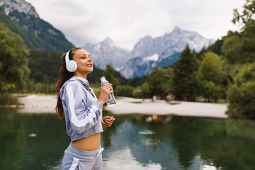 Young sports woman drinks water after workout near the lake