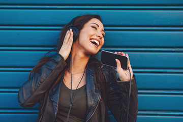 Young woman enjoys music on the street against blue wall