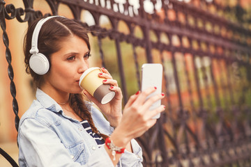 Young woman listens to music via headphones and smartphone in the city