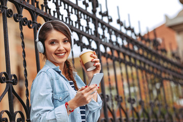 Young woman listens to music via headphones and smartphone in the city