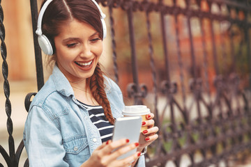 Young woman listens to music via headphones and smartphone in the city