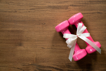 two pink dumbbell with white gift bow on a wooden table background, sport and healthy concept