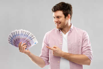 money, finance, business and people concept - smiling young man showing fan of five hundred euro bank notes over grey background