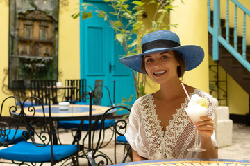 Woman wearing blue hat is enjoying her cold cocktail in city cafe