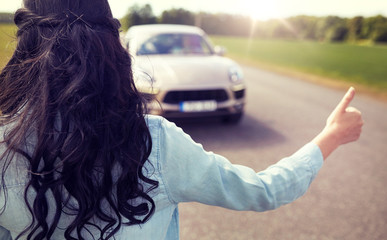 road trip, travel, gesture and people concept - woman hitchhiking and stopping car with thumbs up gesture at countryside 