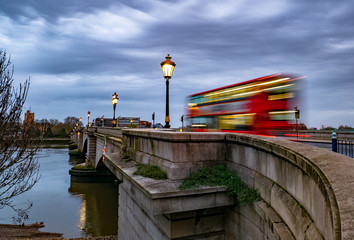 Putney bridge early in the morning at twilight and public transport by traditional red bus in motion in London, UK