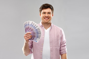 money, finance, business and people concept - smiling young man with fan of five hundred euro bank notes over grey background