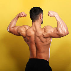 Portrait of young handsome  muscular bodybuilder on black background  with hands on neck view 