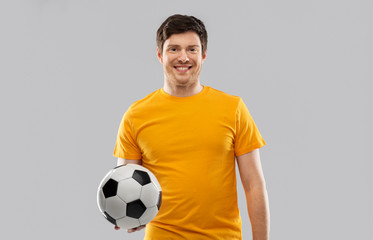 sport, leisure games and people - happy man or football fan in yellow t-shirt with soccer ball over grey background