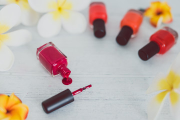 red nail polish bottle and other colors on wooden surface with flowers around it
