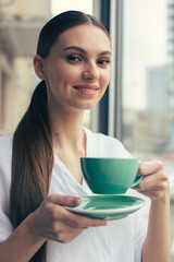 Portrait of smiling woman holding cup of tea above the plate