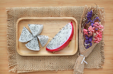 Fresh sliced dragon fruit on wooden tray and sack against wooden board background.
