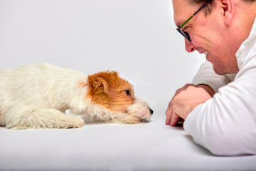 Portrait of happy man lying on floor, playing with adorable jack russell terrier puppy at empty studio interior on white background. Pet lover concept