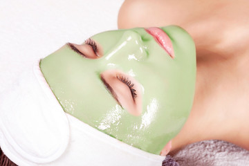 Young beautiful woman with moistening seaweed facial mask at beauty salon.