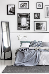 Mirror next to bed with grey sheets in white minimal bedroom interior with posters. Real photo