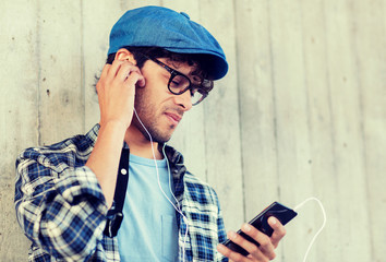 people, music, technology, leisure and lifestyle - happy young hipster man with earphones and smartphone listening to music