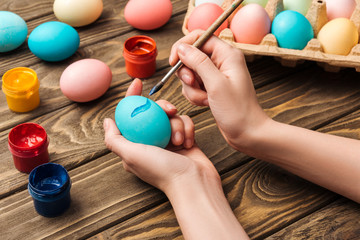 cropped view of woman decorating easter eggs with paintbrush at wooden table