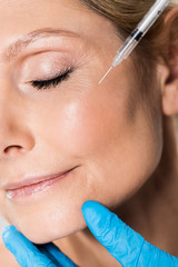 close up of beautiful and mature woman with closed eyes getting beauty injection