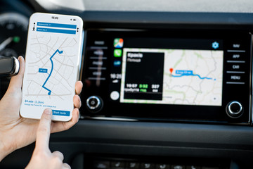 Close-up of a smartphone with navigation app in the modern car with monitor on the background