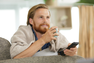 young man drinking tea and watching tv on the sofa