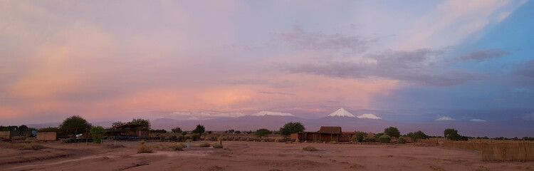 Sunset lights in the arid and desolate landscape of the Atacama Desert and the peaks of the snowy volcanoes of the Andes cordillera in the background