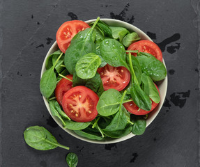 spinach and tomato salad in a bowl on grey stone board. Top view