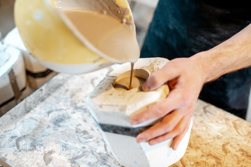 Worker pouring special liquid into the gypsum form making ceramic products at the pottery manufacturing, close-up view