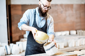 Handsome worker pouring special liquid into the gypsum form at the pottery manufacturing