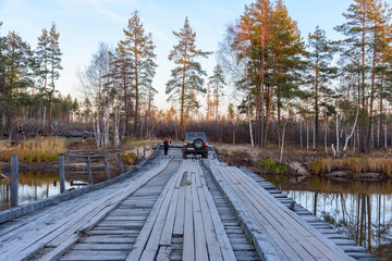 SUV moves on a wooden bridge over a river in the forest