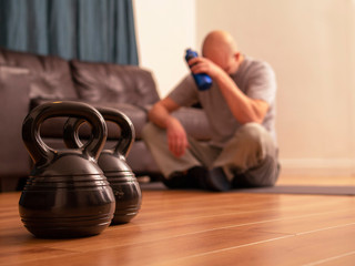 Fitness concept at home, kettle bells in focus, bold man is thinking of something during a break. Get fit home.