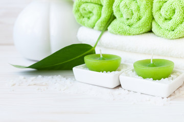 Green plant leaf, aromatic sea salt, candles, vase and towels. Concept for spa, beauty and health salons. Close up photo on white wooden background, selective focus