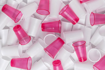 The texture of randomly scattered white and pink disposable plastic cups. Abstract background of plastic dishes.