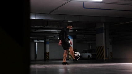 Underground parking lot. A soccer man training his football skills. Balance the ball on his feet