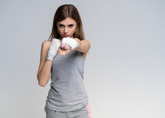 Beautiful boxer girl wearing sportive clothing and gloves practicing in the studio over gray background, athletic body, healthy lifestyle.
