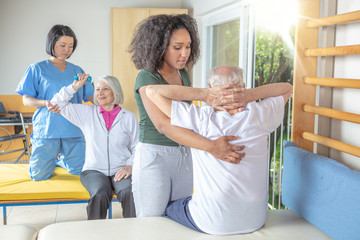 Couple of nurses helping active senior couple at rehab gym. Retirement community concept