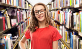 education, school and people concept - smiling teenage student girl in glasses and red t-shirt over book shelves in library background