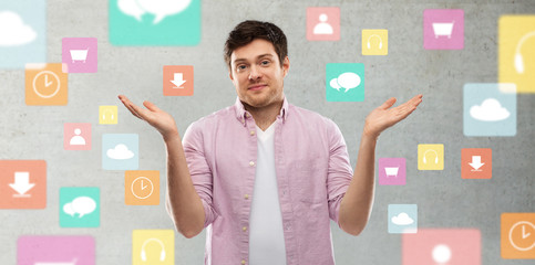 people, technology and expression concept - young man shrugging over app icons on grey background