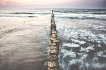 Wooden sea breakwater at sunset, color toning applied, long exposure.