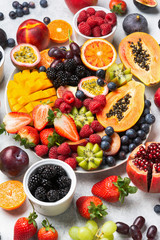 Healthy rainbow fruit platter mango papaya strawberries oranges passion fruits berries on oval serving plate on white concrete kitchen top background, selective focus