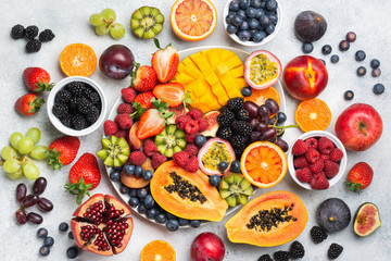 Healthy raw rainbow fruit platter mango papaya strawberries oranges passion fruits berries on oval serving plate on light concrete background, top view, selective focus