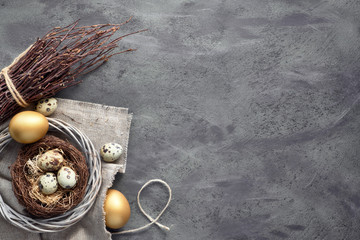 Easter flat lay on dark background with quail eggs in the nest, linen fabrique and two golden eggs on dark with copy-space