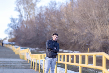 A young man in a black jacket on the background of spring trees in Cheboksary