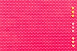 Yellow and pink small hearts on the right vertical line on the textile background, fuchsia with a print in white polka dots. View from above.