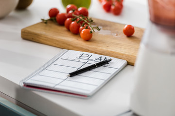 selective focus of notebook with plan lettering near wooden cutting board with cherry tomatoes