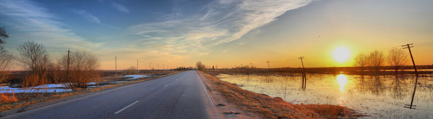 Panorama of the road between the fields with spring flood