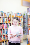 girl of 13 years old choosing book in library.