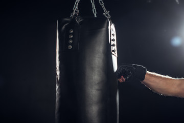 Partial view of boxer training with punching bag on black
