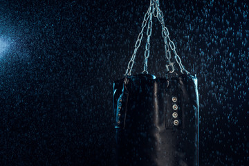 Leather punching bag hanging on steel chains under water drops on black